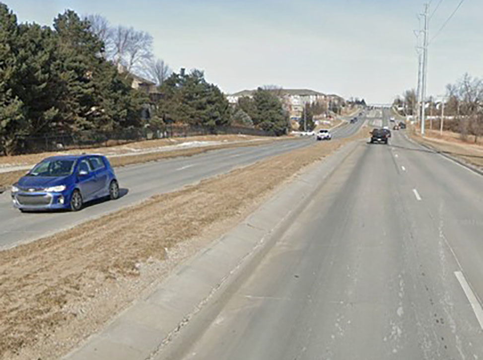 Street view image of 168th Street with cars on the road, trees along the side and apartments in the distance.